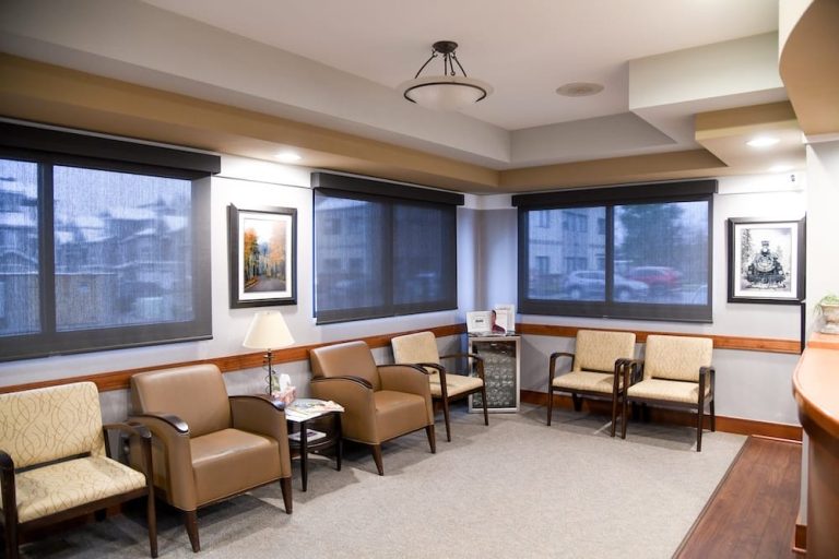 A clean, empty waiting room in Fort Collins features several chairs, framed artwork on the walls, large windows with shades, and a small table with magazines. Warm lighting creates a welcoming atmosphere.