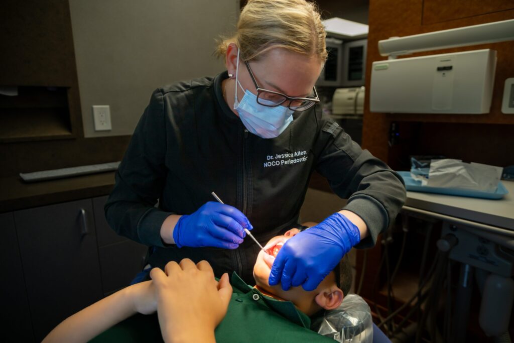 A dentist wearing gloves and a mask examines a young patientâ€™s teeth in a dental clinic, checking for conditions that may require procedures like a frenectomy. The child lies back in the chair while the dentist uses dental instruments.